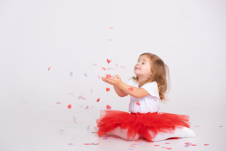 toddler girl on red skirt throws confetti on a white backgroundの写真素材