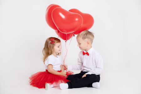 little boy giving heart balloons to toddler girl on valentines day on white backgroundの写真素材