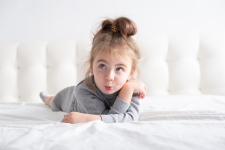 little girl in gray turtleneck having fun on white bedding.の写真素材