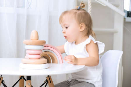 Child girl playing with a wooden toys at table. Little cute girl with natural toys