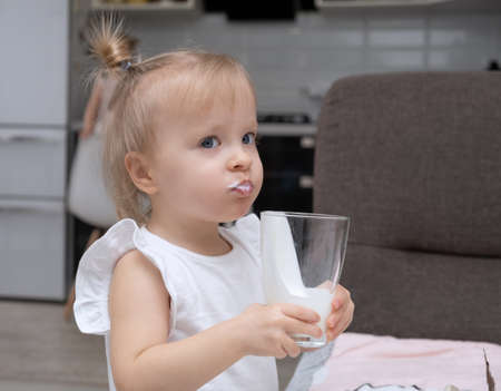 cute little blonde girl drinking organic milk, holding glass at home kitchen.の写真素材