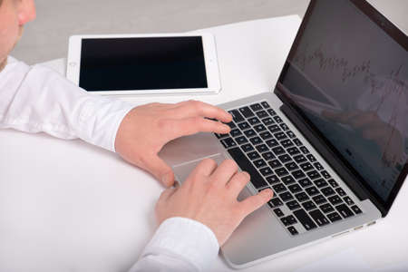 man hands using laptop and tablet with charts, businessman sitting at table and working.