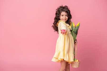 beautiful child girl holding basket with easter eggs and tulips on pink background.の写真素材