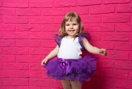carefree cute little girl in tutu skirt laughing out loud giggling on pink background.の写真素材