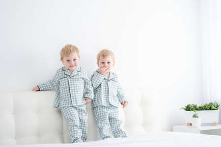 Two happy boys brothers on white bed in pajamas, having fun together, laughing, playing.の写真素材