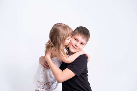 cute little sister kissing hugging her handsome older brother teenager on white backgroundの写真素材