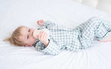 toddler baby boy in pajamas lie on bed drinking milk from bottles. Candid home childhood life.の写真素材