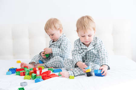 Two funny boys brothers twins on white bed in pajamas playing in constructorの写真素材