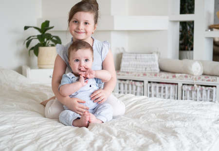 cute little girl older sister with her baby boy brother at home sitting on bed.
