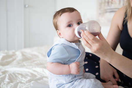 Young mother feeding her little baby boy from bottle in bed. mom gives her baby a drink.