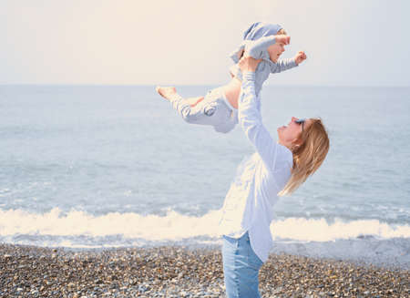 mother throw little son in air, family having fun on shore of sea on sunny day