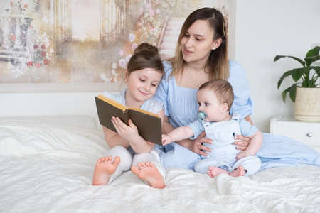 mother reads a book with two children baby son and little girl daughter in bed.の写真素材