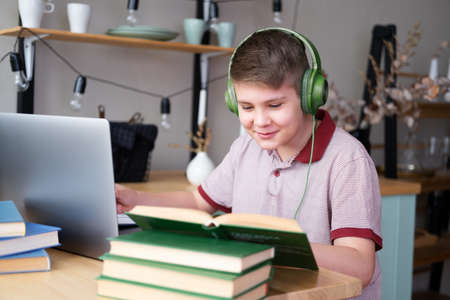 teenager boy in headphones studying online using laptop writing in notebook, reading book.の写真素材