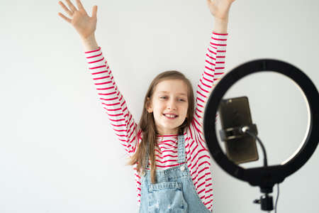 Teenage girl social media blogger recording video speaking looking at smartphone on tripod with ring...