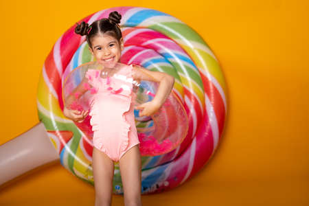 Cute arab little girl in swimming suit and swimming inflatable ring smiling having fun on yellow backgroundの写真素材