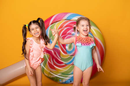 two cute child girls in swimming suit laughing having fun on yellow background with lollipop.の写真素材