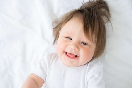 portrait of funny baby boy 6 month smiling and lying on a white bedding at home