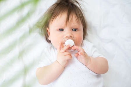 cute baby boy 6 month with nipple lying on a white bedding at home. top view