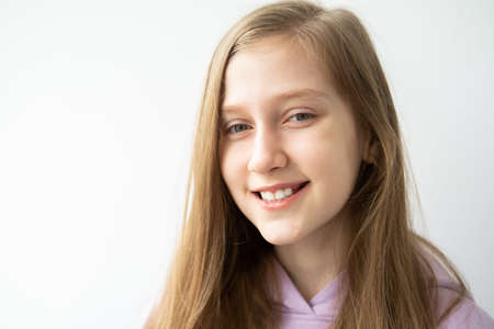 portrait of beautiful teenage girl with long hair in purple huddy standing against white wall.