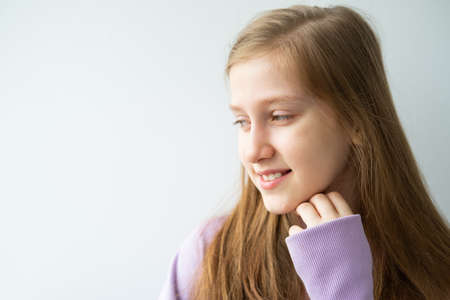 portrait of beautiful teenage girl with long hair in purple huddy standing against white wall.