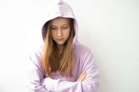 close up hooded upset girl with long hair in purple hoodie standing against white wallの写真素材