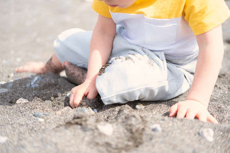 little blonde boy playing with rocks and sand on the beach on a sunny day.の写真素材