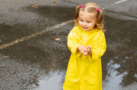 Cute blonde baby girl toddler wearing yellow stylish raincoat closeup. childhoodの写真素材
