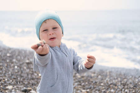 child blond boy playing with rocks and sand on the beach on a sunny day in spring or autumn