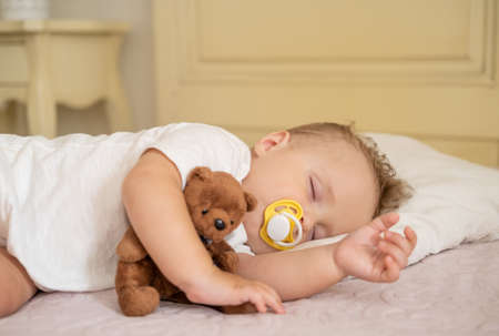 cute baby boy with nipple sleeping on bed at home. child hugging teddy bear.の写真素材
