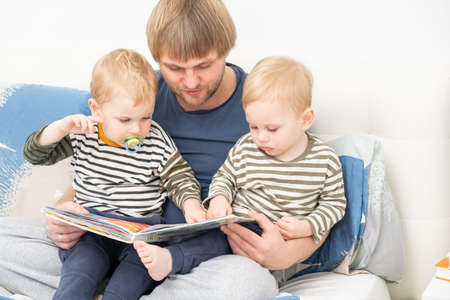 father reading a book to his sons twins on bed at home, spending time together.の写真素材