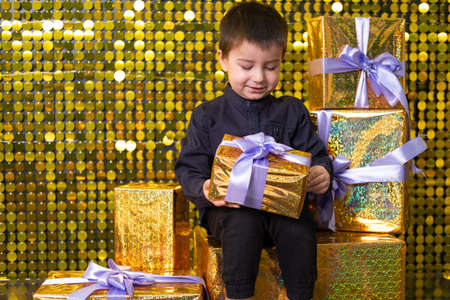 child smiling boy holding gift box on background with gold shiny sequins, paillettes.の写真素材