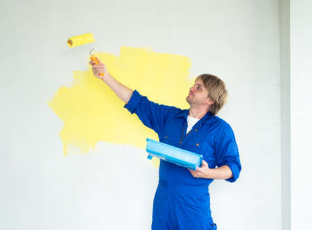 man painting wall in yellow color with roller. Renovation, repair and redecoration concept.の写真素材