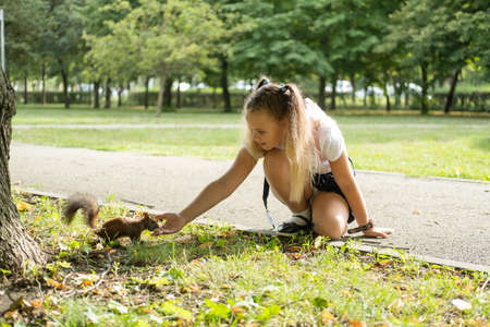happy schoolgirl in uniform with backpack feeds a squirrel in the park on her way to school.