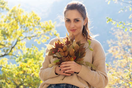 attractive happy middle aged woman in sweater holds bouquet of colorful leaves. autumn season.の写真素材