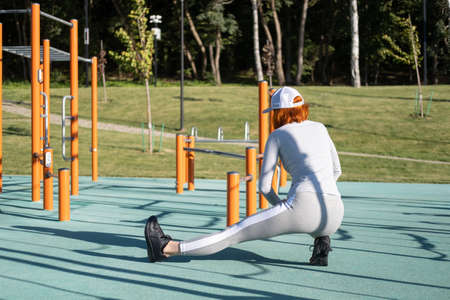 athletic ginger woman warming up for morning training outdoor on urban sports ground in autumn sunny dayの写真素材