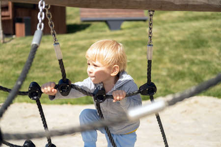 Little caucasian blond boy playing on kids playground in a sunny autumn day.の写真素材