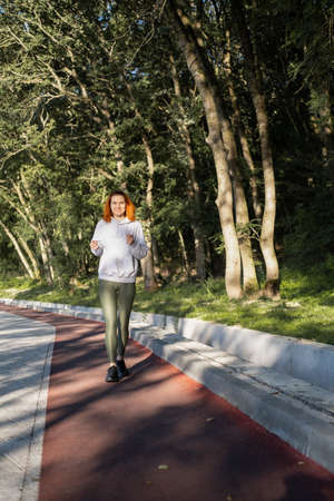 slim ginger woman in sport clothes running in park on morning. Healthy fitness lifestyle.
