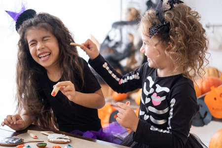 two diverse kids girl in costume of witch, having fun at home in kitchen, celebrating Halloween.の写真素材
