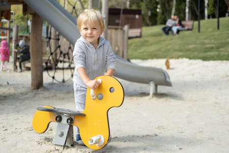Little caucasian blond boy playing on kids playground in a sunny autumn day.の写真素材