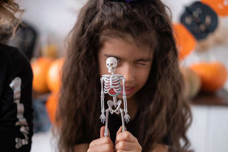 cute girl in witch costume witch having fun in kitchen, playing with skeleton, celebrating...