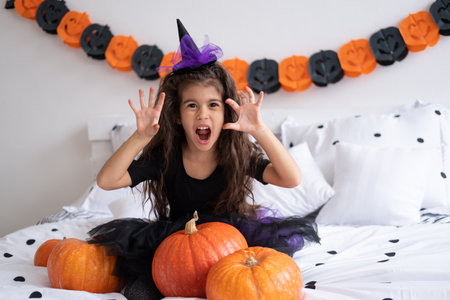 funny arabic kid girl in witch costume having fun in decorated for halloween bedroom.の写真素材