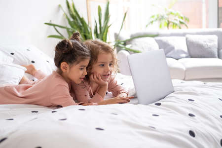 cute little kids girls in pajamas using laptop in bed at home. Kids using technology.の写真素材
