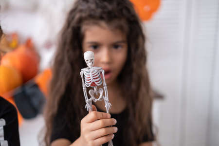 cute girl in witch costume witch having fun in kitchen, playing with skeleton, celebrating Halloween. selective focus.の写真素材