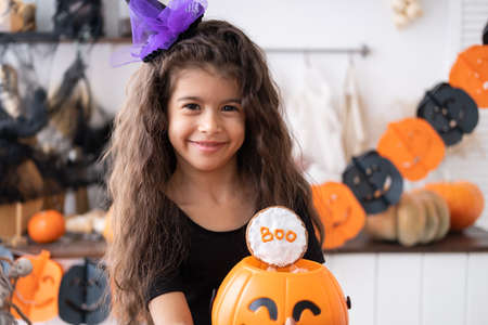 cute little girl in costume of witch holding pumpkin jack with candies, having fun in kitchen, celebrating Halloween.の写真素材