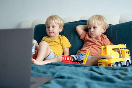 cute little caucasian kids boys twins using laptop in bed at home. Kids using technology.の写真素材