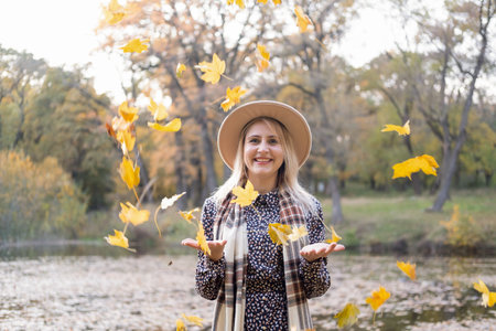 happy blonde woman throwing autumn leaves in the air in autumn park in fallの写真素材