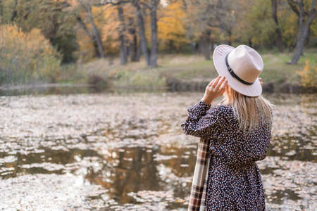rear view of beautiful woman in fashion clothes and hat by the lake in autumn park in fall.の写真素材