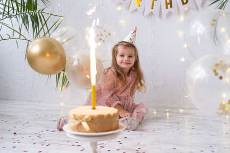 happy cute little child girl sitting with birthday cake with burning candle and celebrating birthdayの写真素材