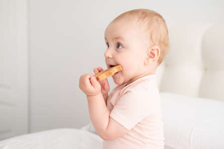 baby girl in light pink bodysuit nibbling wooden toys on white bedding on bedの写真素材