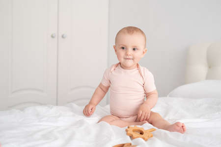 baby girl in light pink bodysuit playing with wooden toys on white bedding on bedの写真素材